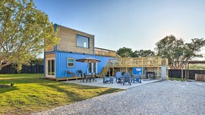 Un jardin avec une maison conteneur bleue, du mobilier d’extérieur et une terrasse en bois.