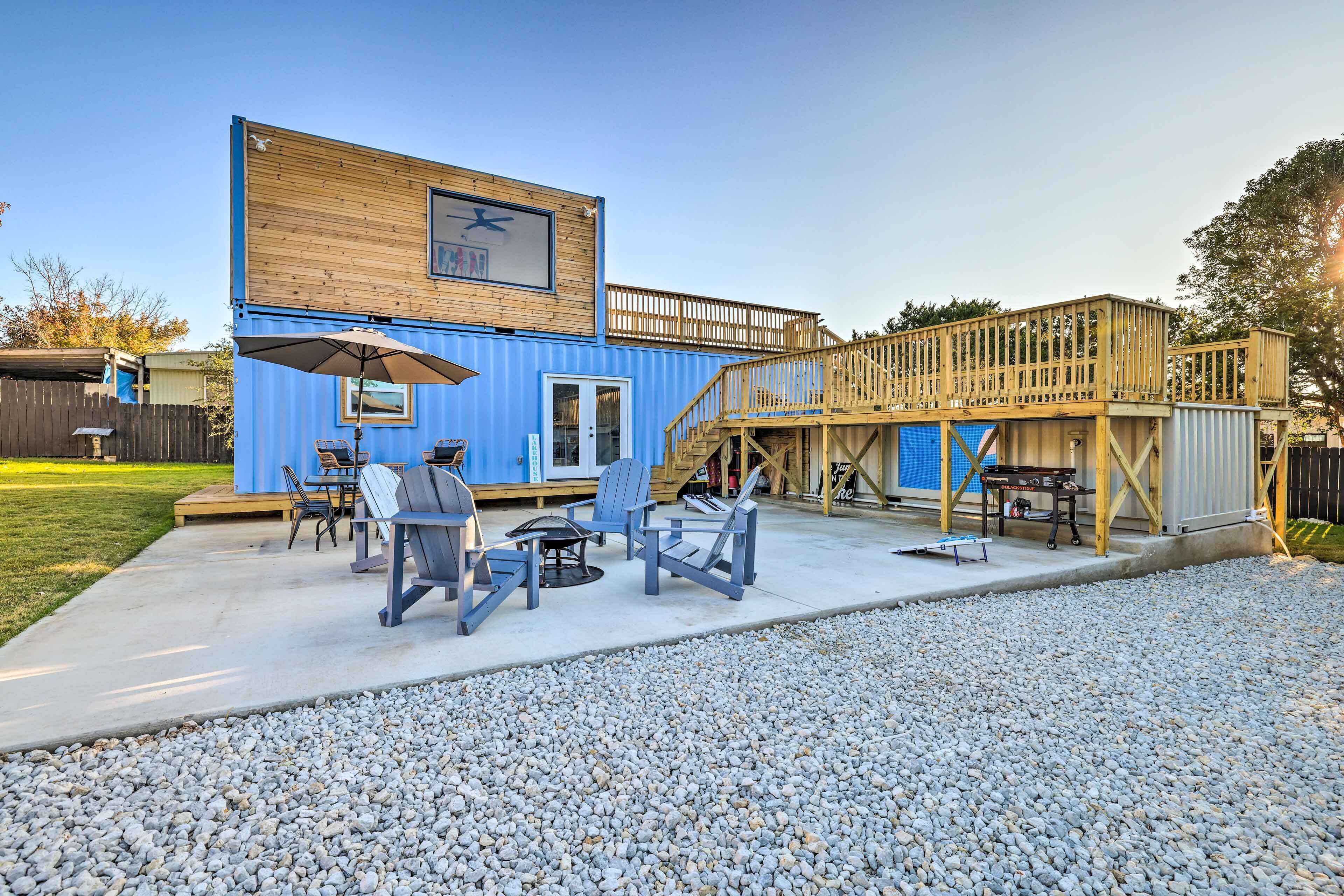 A blue container house with a wooden deck, outdoor seating area, and a staircase to the upper level.