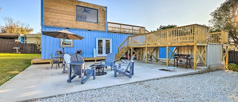 Une maison conteneur bleue dotée d’une terrasse en bois, d’un espace salon extérieur et d’un escalier menant à l’étage supérieur.