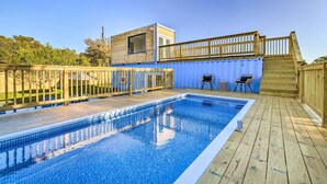 Une piscine avec une terrasse en bois, une petite structure en bois dotée d’une fenêtre et un espace clos avec des chaises.