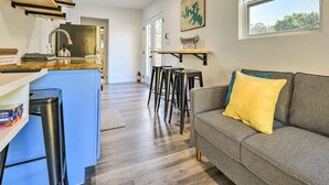 Une cuisine moderne dotée d’un îlot central, de tabourets de bar et d’un canapé gris agrémenté d’un coussin jaune.