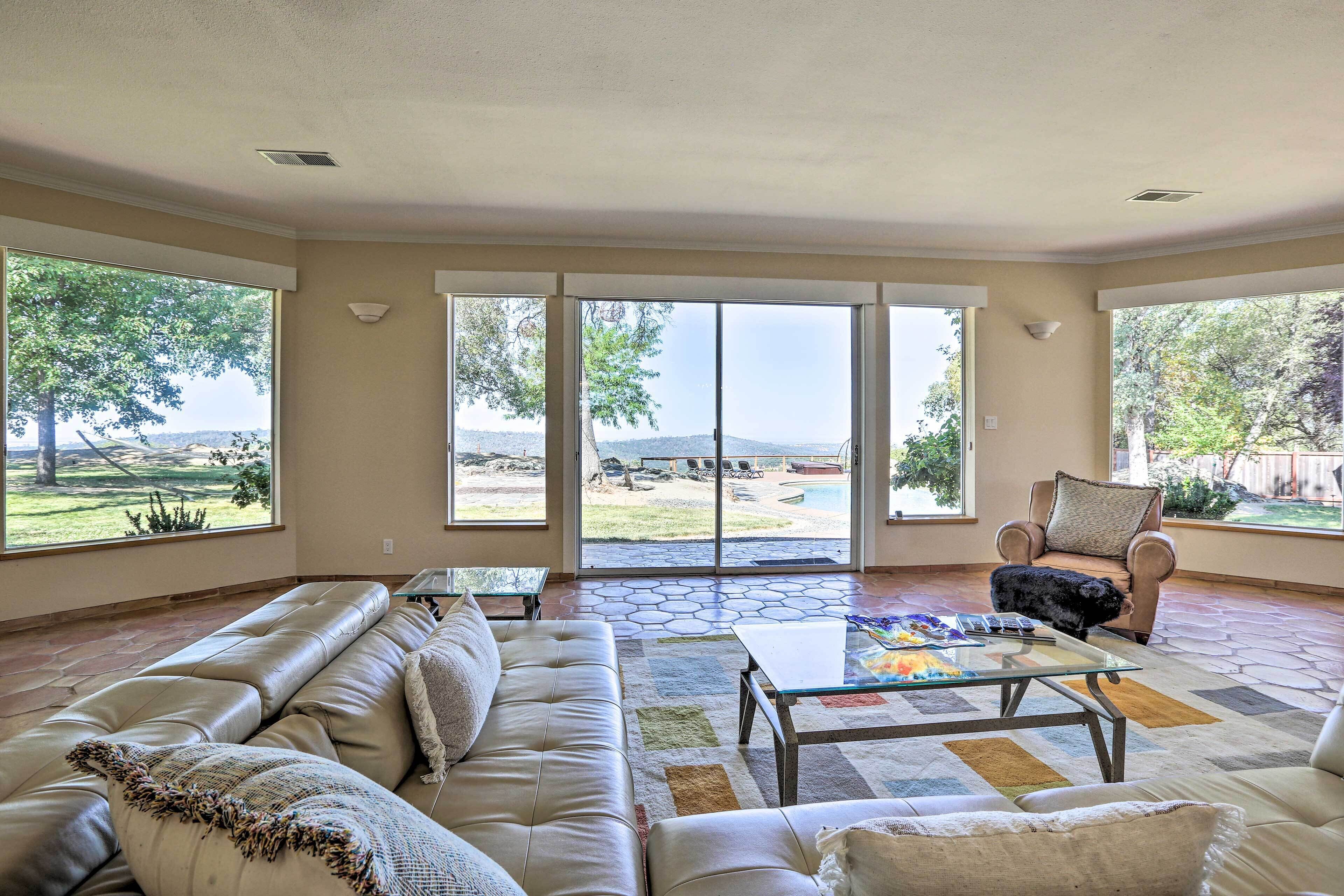 A spacious living room with a leather sofa, a coffee table, and a view of a backyard through large sliding glass doors.