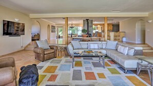 A spacious living room with a large sectional sofa, a coffee table, and a colorful rug. There is a dog in the foreground. - Luxe Auburn Hideaway w/ Tennis Court & Views! (Auburn)