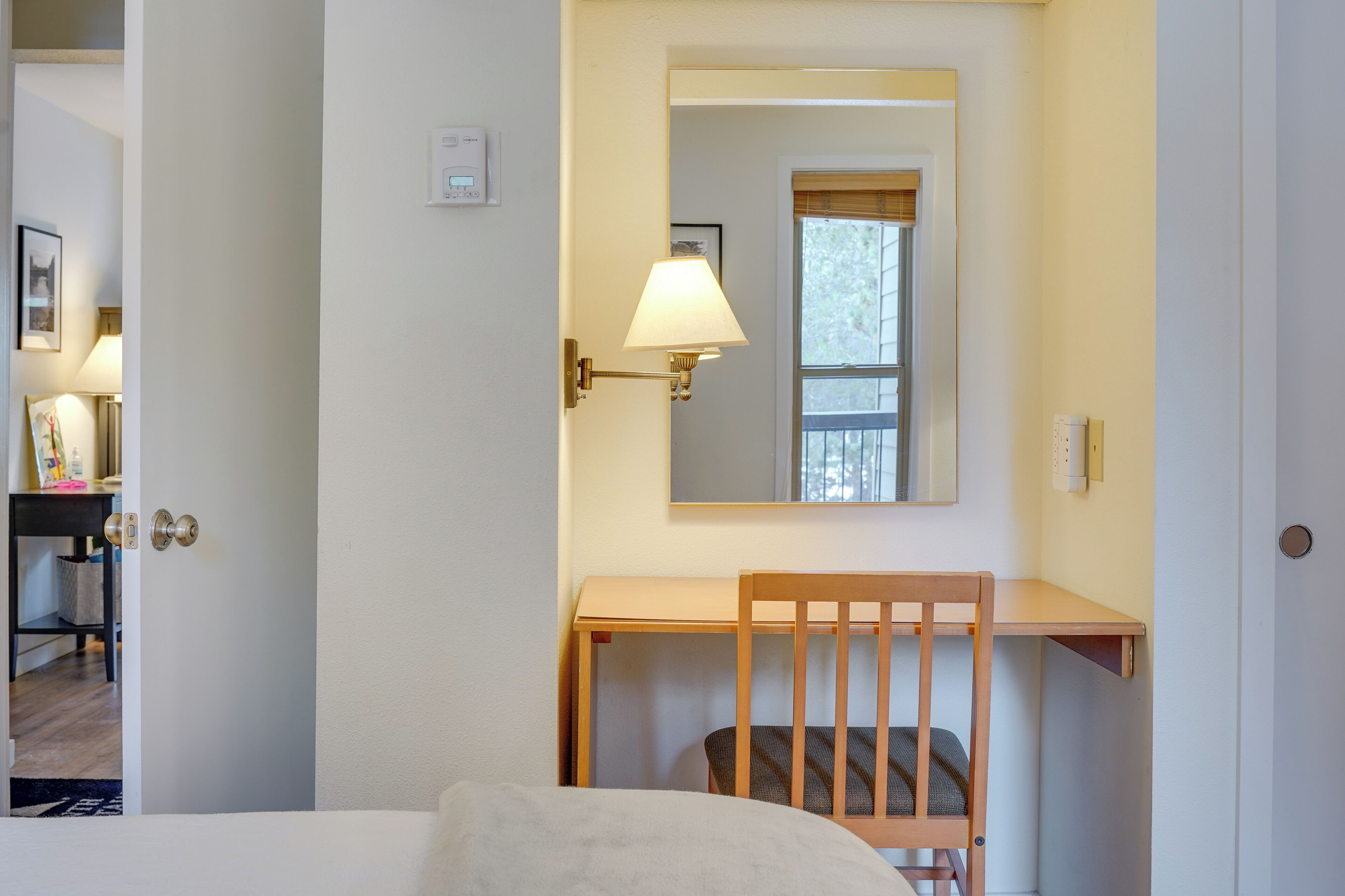 Une chambre d’hôtel avec un bureau en bois, une chaise, un lit et une lampe fixée au mur.
