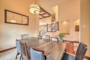 A dining area with a large wooden table, six chairs, a hanging light fixture, and a staircase in the background. - Spacious Kirkland Home 15 Mi to Dtwn Seattle! (Kirkland)