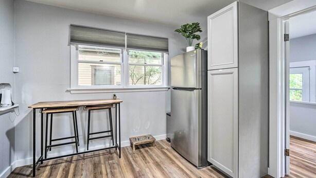 A kitchen with a stainless steel refrigerator, a wooden table with two stools, a small plant on top of the refrigerator, and a window with blinds. - Charming Fort Collins Home By Old Town & Csu! (Fort Collins)