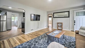 A modern living room with a wooden floor, a grey patterned rug, a wooden coffee table, a beige sofa, and a flat-screen TV mounted on the wall. - Charming Fort Collins Home By Old Town & Csu! (Fort Collins)