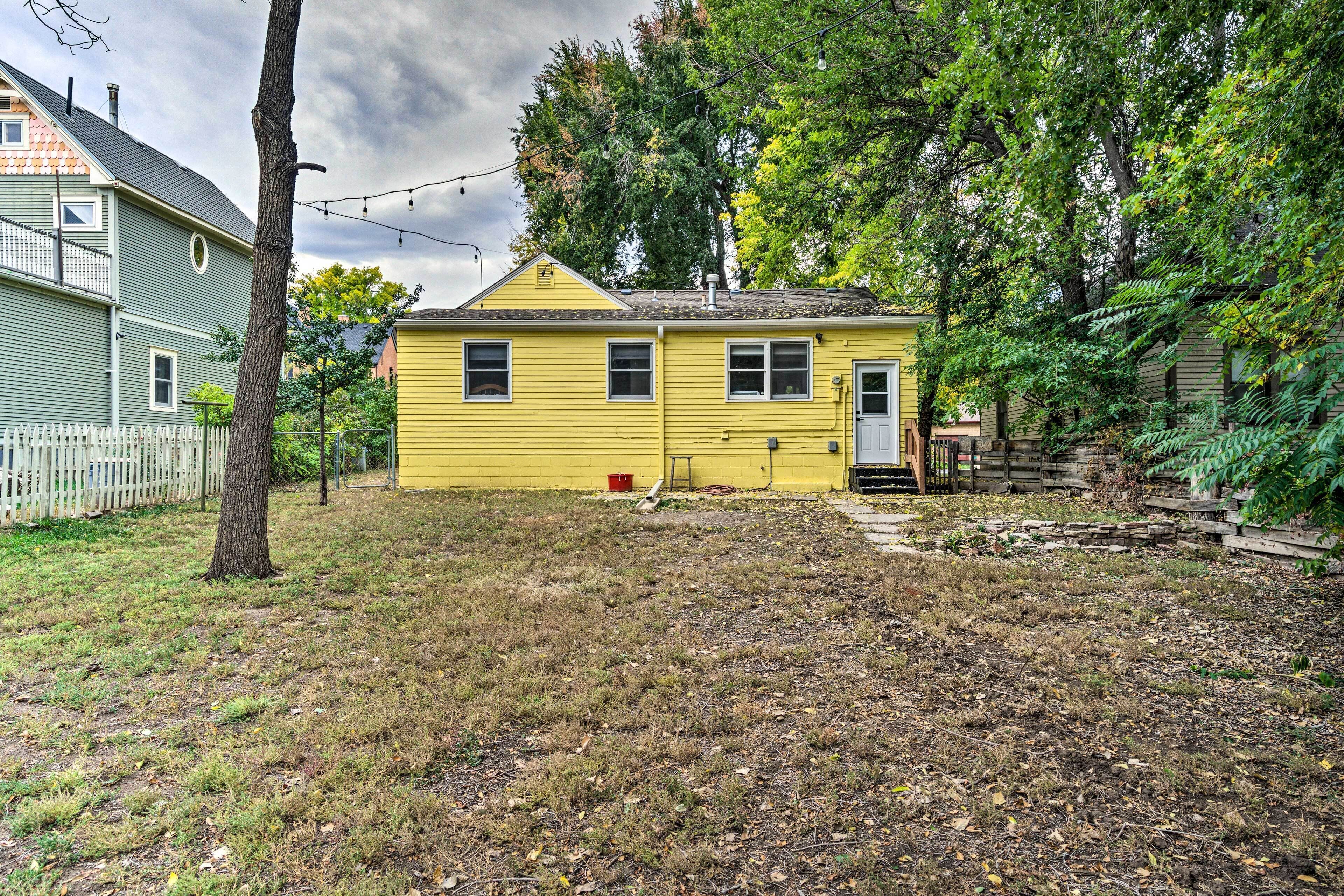 A yellow single-story house with a white door and windows, surrounded by a grassy yard and trees.