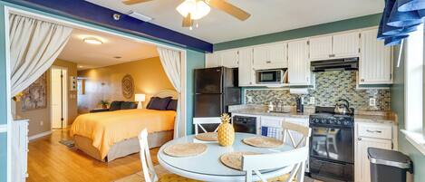 A compact kitchen with white cabinets, a microwave, a stove, and a ceiling fan.