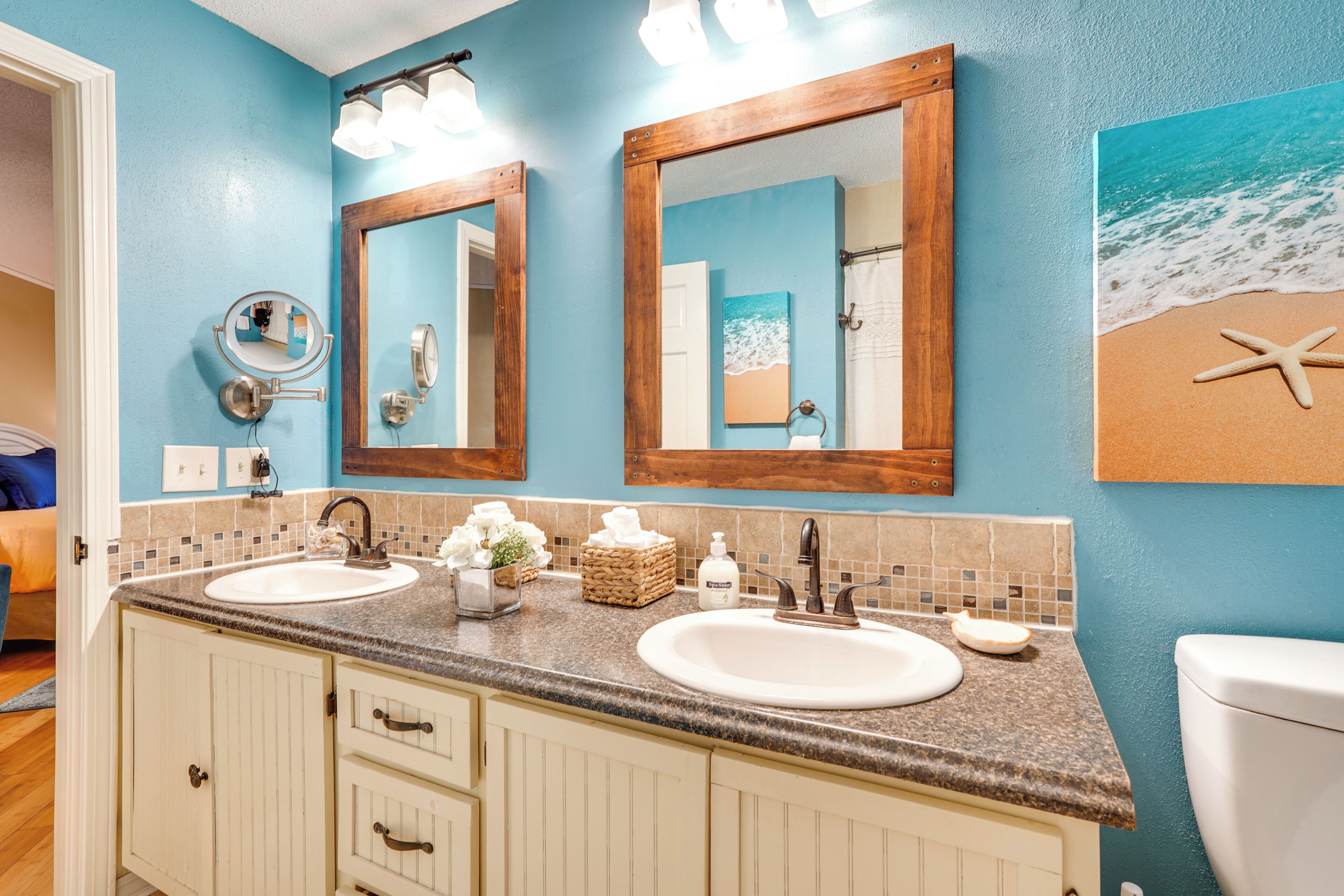 Un baño con dos lavamanos, espejos con marco de madera y decoración de temática playera.