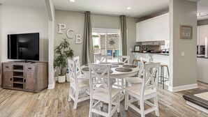 A dining area with a round table, white chairs, a potted plant, and a television on a cabinet. - 'bailey's Beach House Retreat' w/ Game Room! (Panama City Beach)