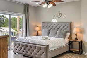 A bedroom with a tufted headboard, two bedside lamps, and a view through a sliding glass door. - 'bailey's Beach House Retreat' w/ Game Room! (Panama City Beach)