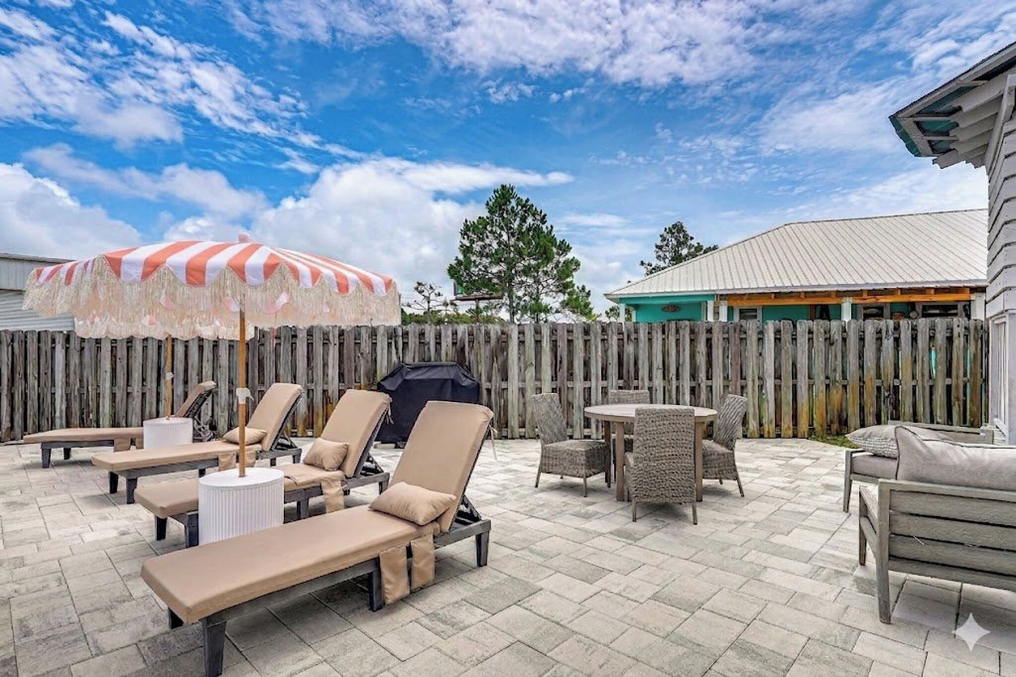 An outdoor patio with lounge chairs, a striped umbrella, and a wooden fence.