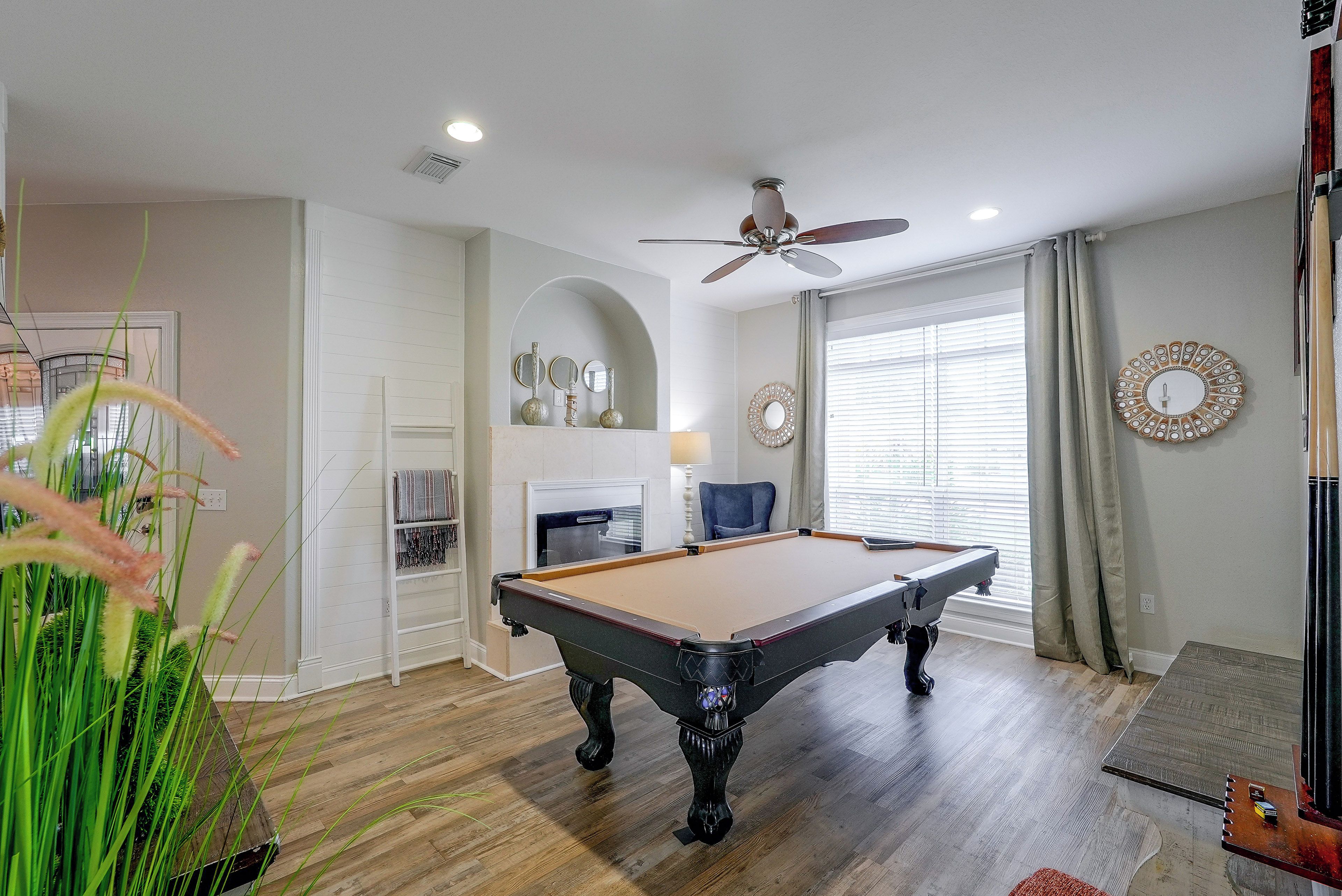 A pool table in a room with a ceiling fan, a fireplace, and decorative mirrors.