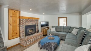 A living room with a brick fireplace, a grey sofa, a television, and a wooden door.