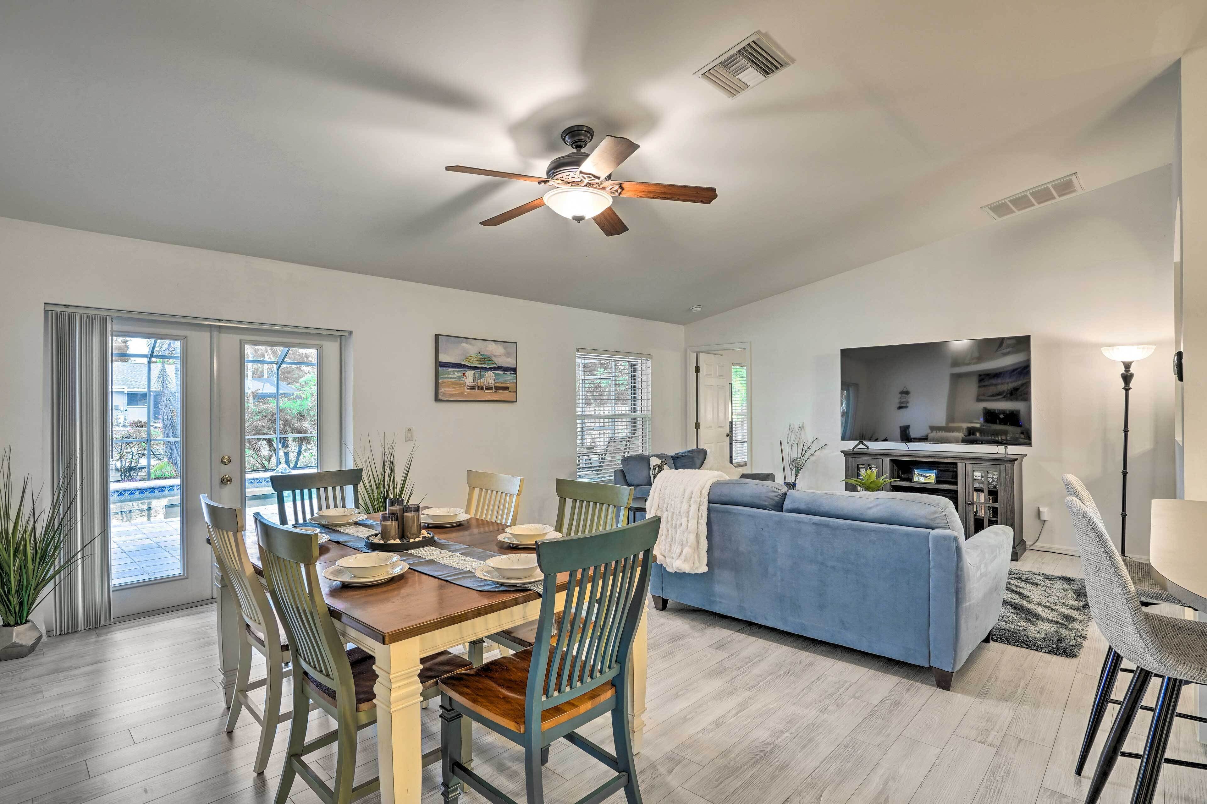 A spacious living room with a blue sofa, dining area with wooden chairs, a ceiling fan, and a kitchen area with a TV.