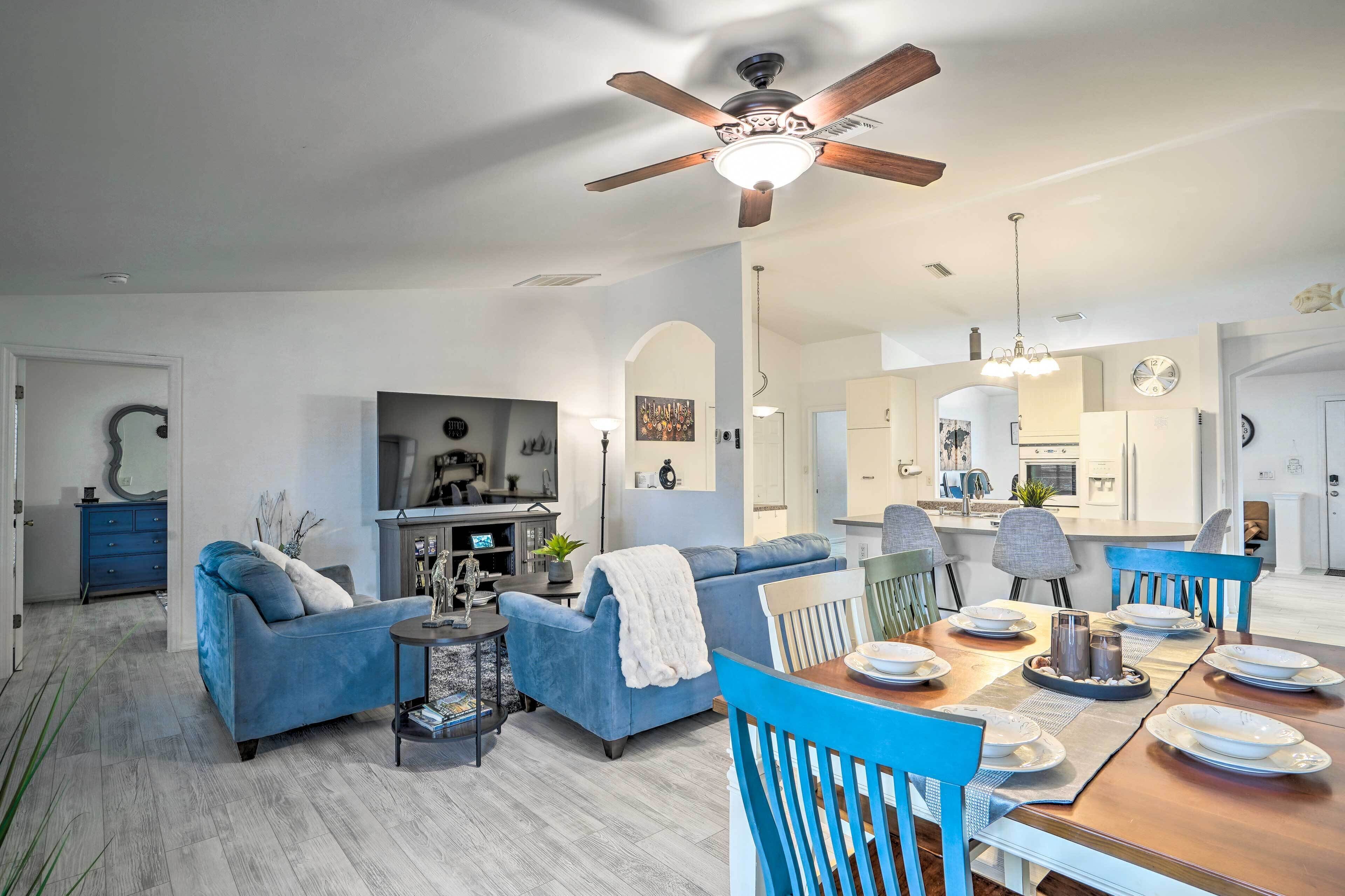 A modern living room with a blue sofa, dining table set for four, and a ceiling fan.