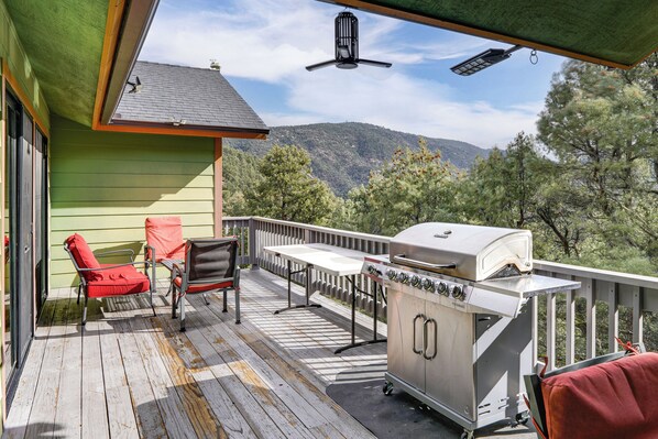 A deck with a grill, chairs, and a view of mountains.