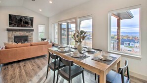 A modern living room with a fireplace, a dining table set for four, and large windows offering a view of the city. - Eden Home w/ Stunning View ~ 6 Mi to Skiing! (Eden)
