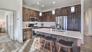 A modern kitchen with dark wooden cabinets, stainless steel appliances, and a large island with bar stools. - Eden Home w/ Stunning View ~ 6 Mi to Skiing! (Eden)