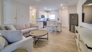 A modern living room with a sofa, coffee table, and a kitchen in the background. - Modern Port St Joe Getaway - Steps to Beach! (Port St. Joe)