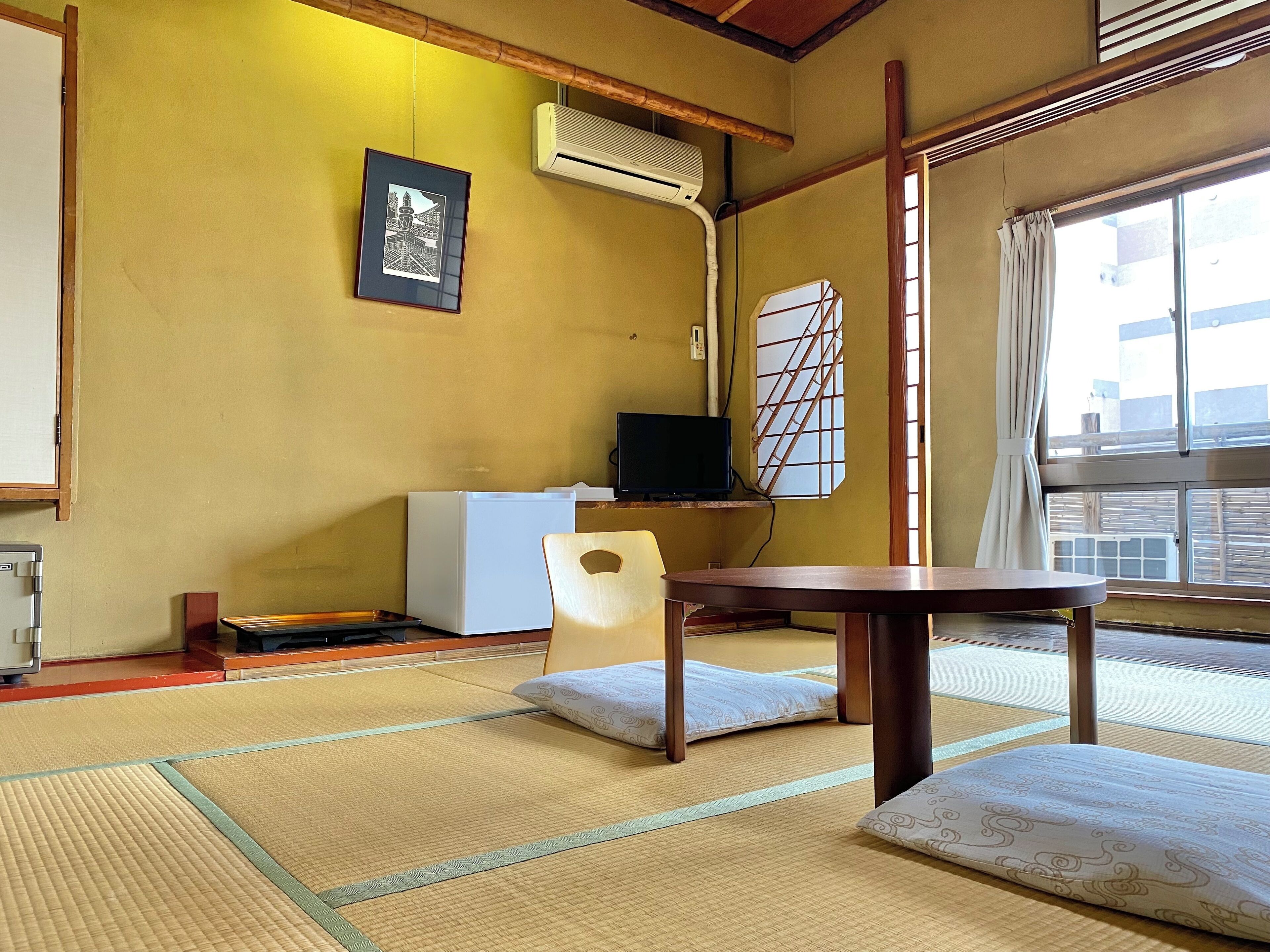 A traditional Japanese room with tatami flooring, a low table, a chair, a television, and a framed picture on the wall.