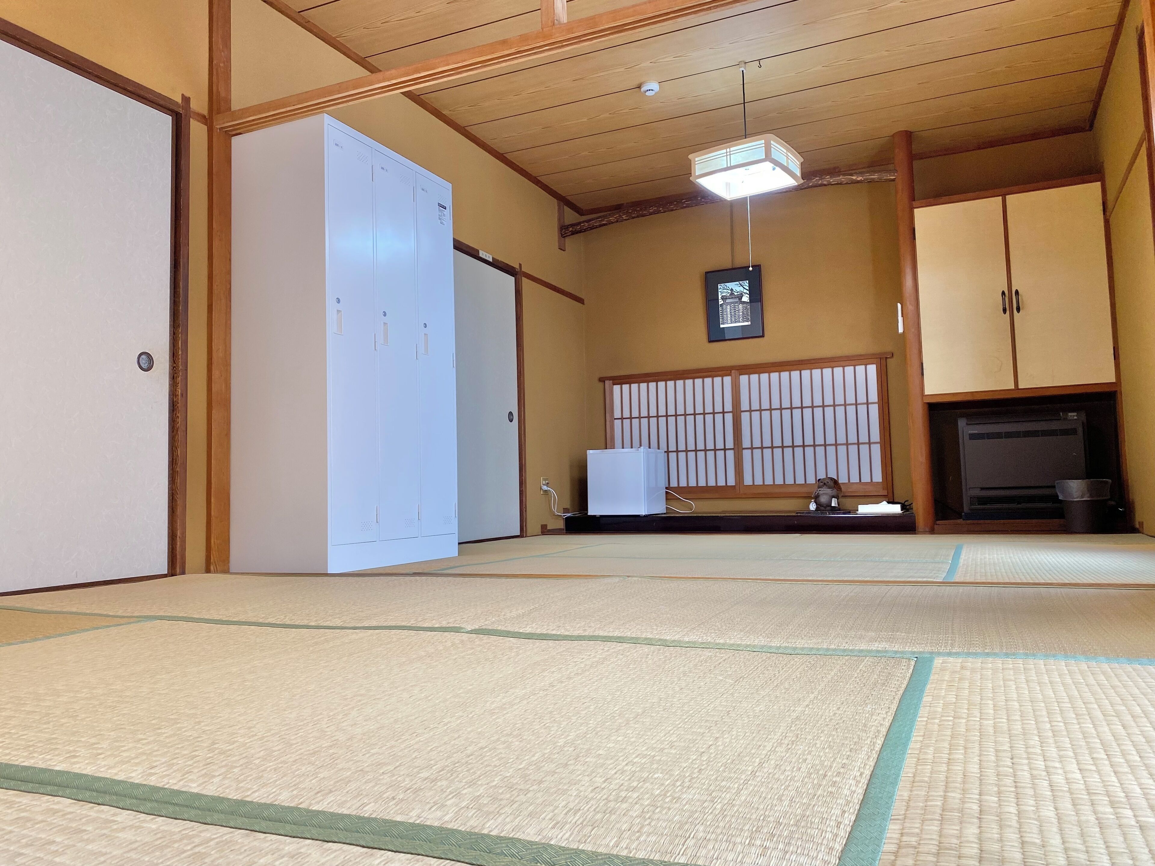 A traditional Japanese room with tatami flooring, a white wardrobe, a small heater, and a television.