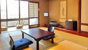 Una habitación japonesa tradicional con suelo de tatami, una mesa baja, una silla, un televisor y un biombo decorativo.