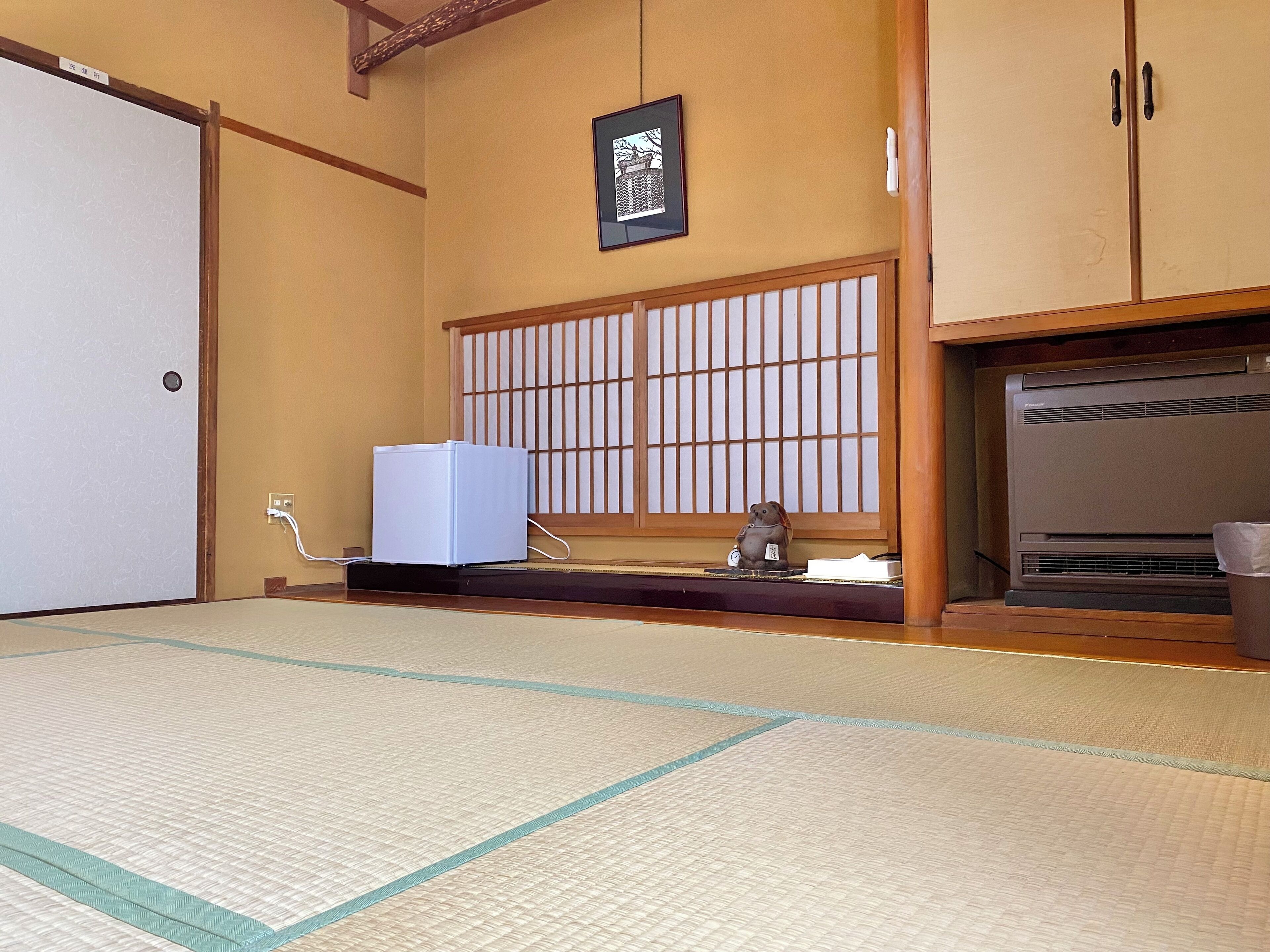 Una habitación con esteras de tatami, un fusuma tradicional japonés, un calentador y una pequeña estatua en un estante.