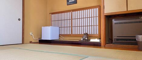 Una habitación con esteras de tatami, un fusuma tradicional japonés, un calentador y una pequeña estatua en un estante.
