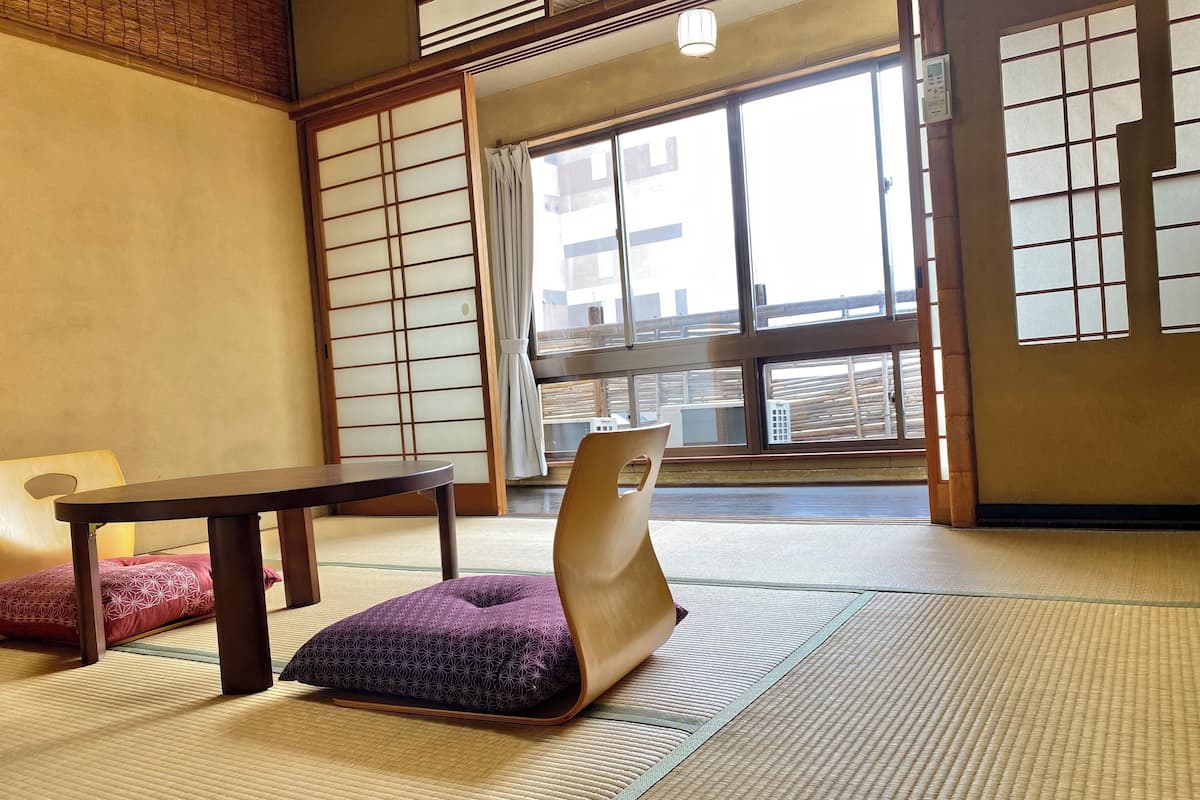 A traditional Japanese room with tatami flooring, a low table, a cushioned bench, and sliding shoji doors.