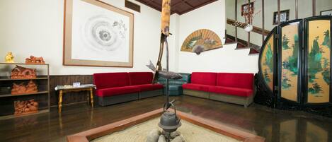 Un interior tradicional con un futón de tatami, asientos rojos, una obra de arte grande enmarcada y un abanico decorativo.
