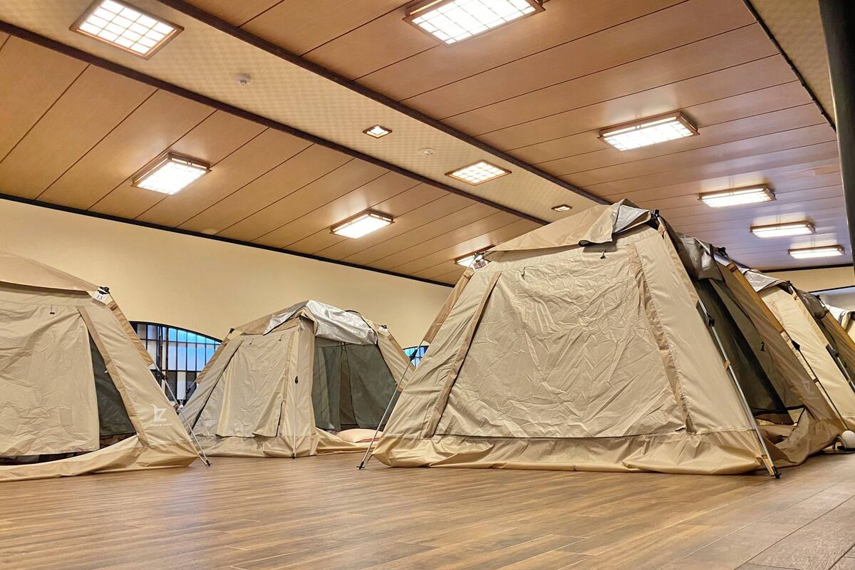 A row of beige tents with a wooden floor and ceiling lights.