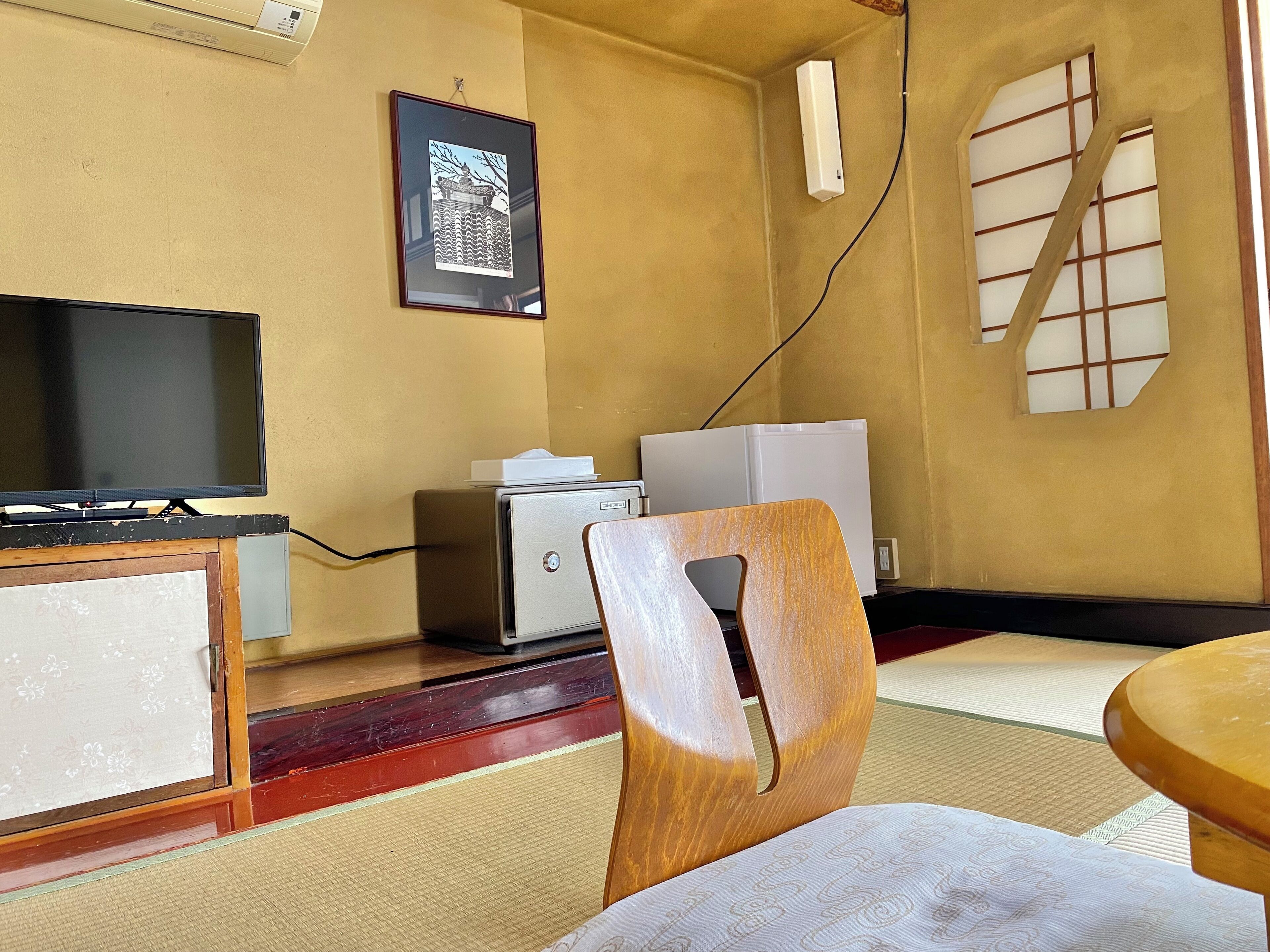 Habitación con televisión, impresora, un cuadro en la pared y piso de tatami japonés tradicional.