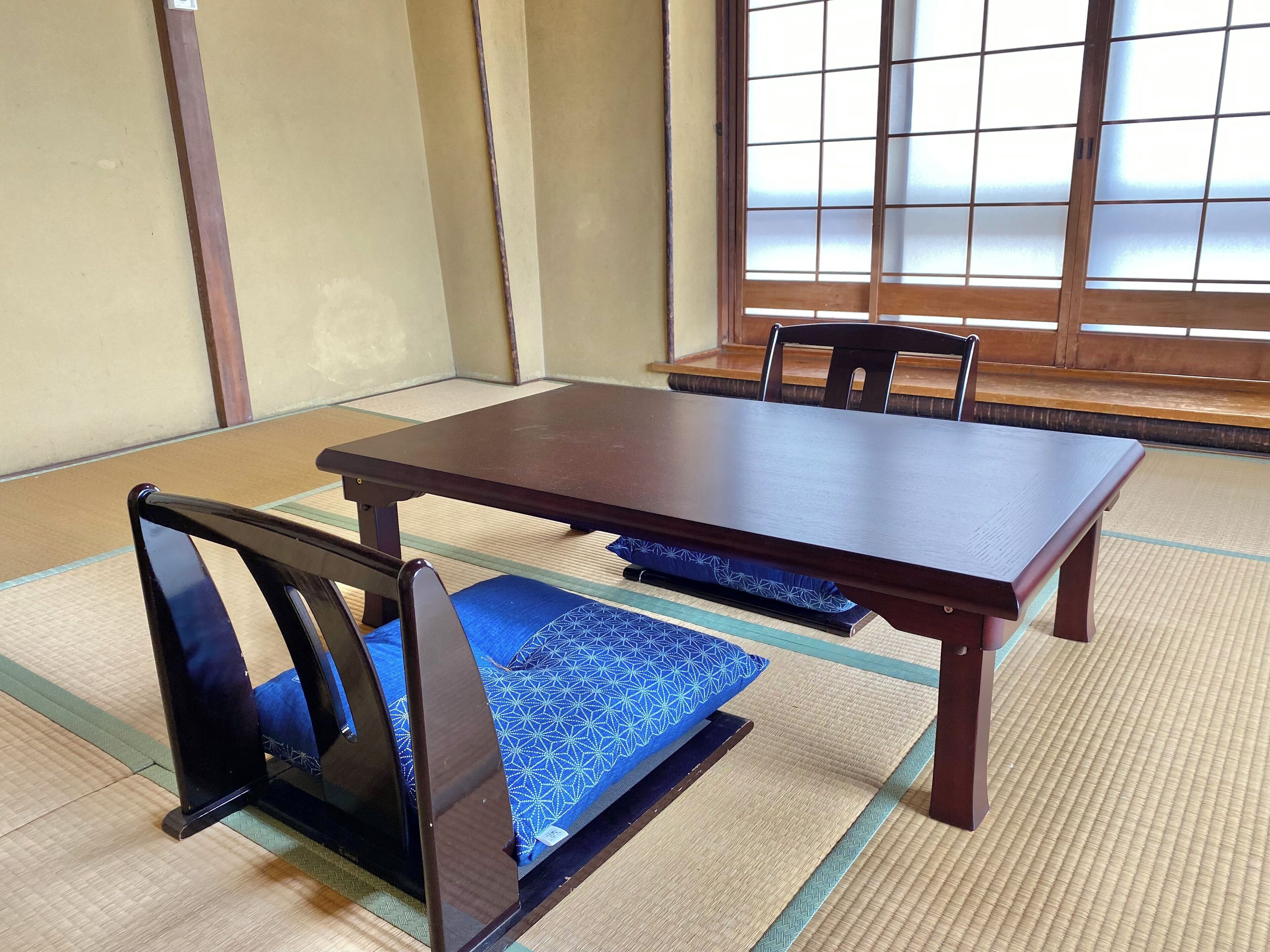 Una habitación japonesa tradicional con suelo de tatami, una mesa de madera baja y sillas negras.