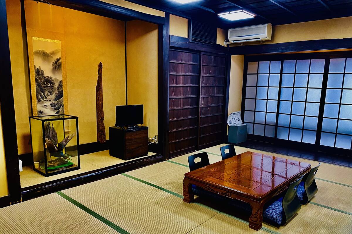 A traditional Japanese room with tatami flooring, a wooden table, a television, and a shoji screen.