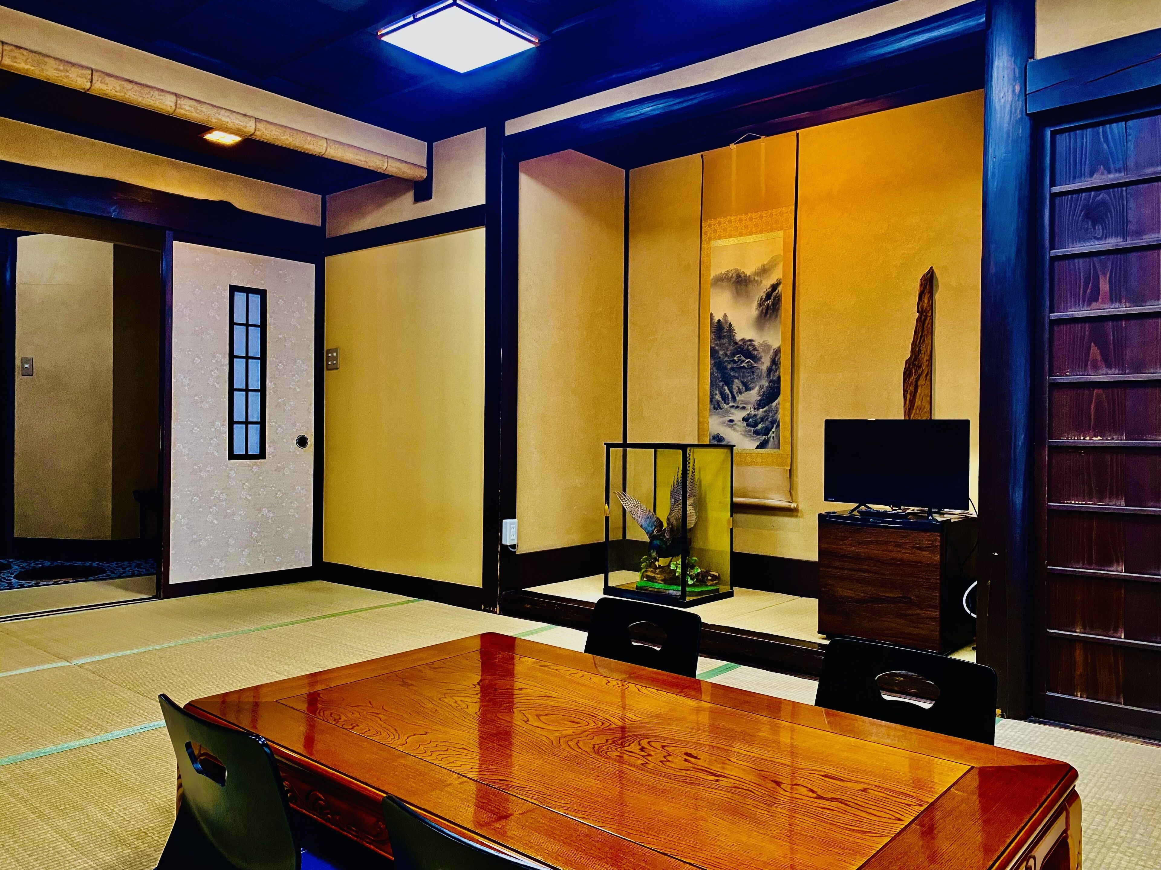 A traditional Japanese-style room with tatami flooring, a wooden table, and a television.
