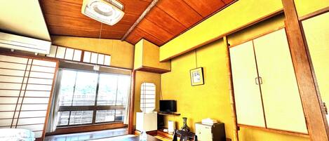 A traditional Japanese room with tatami flooring, a wooden ceiling, and a sliding door leading to a balcony.