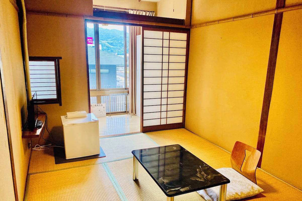 A traditional Japanese room with tatami flooring, a black table, a white sofa, and a sliding shoji screen door.