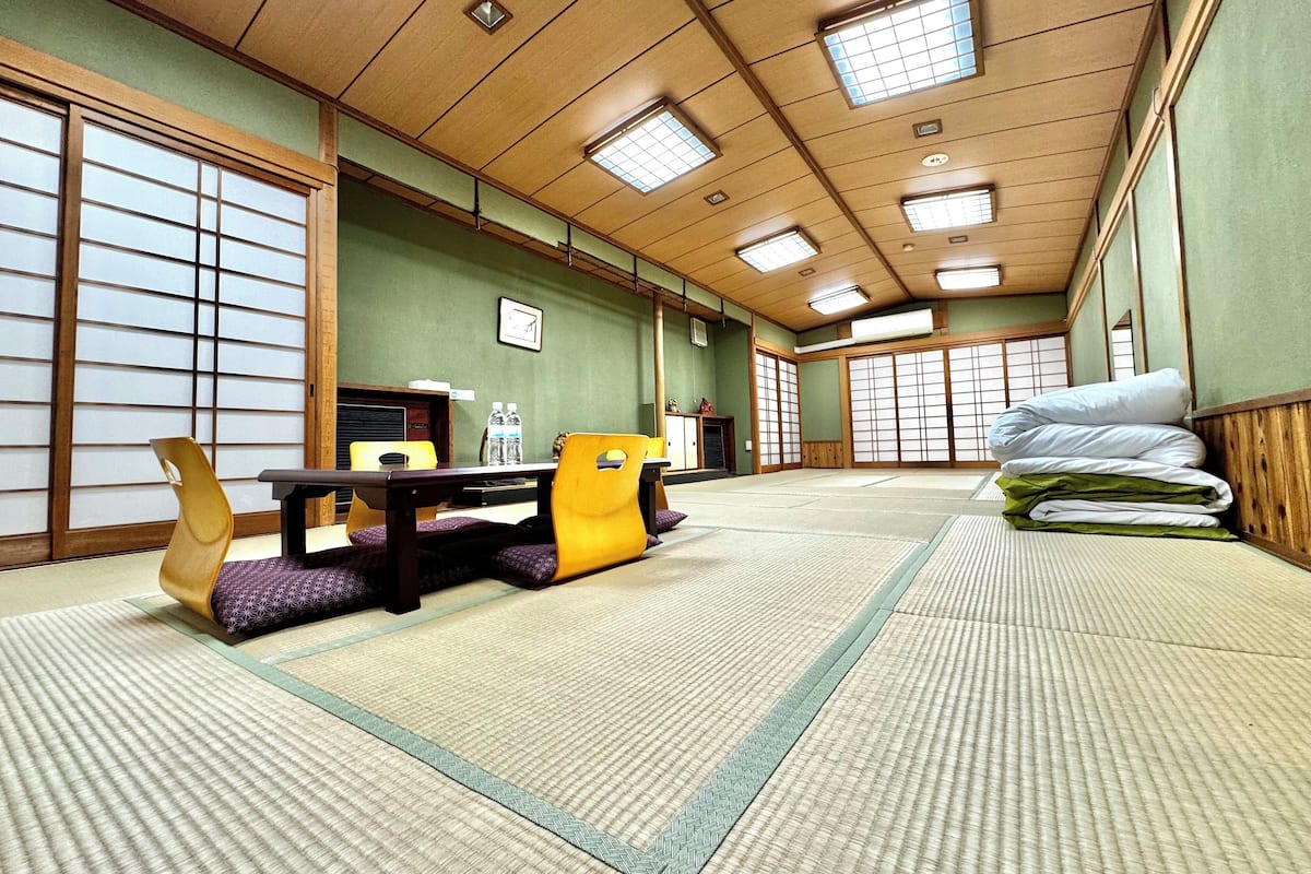 A tatami mat room with a low table, chairs, and a stack of pillows.