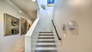 Una escalera con barandilla, apliques de cristal transparente y obras de arte en las paredes.
