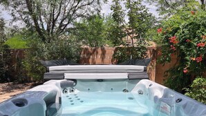 Un jacuzzi con asiento integrado, rodeado por un muro de ladrillo y abundante vegetación.
