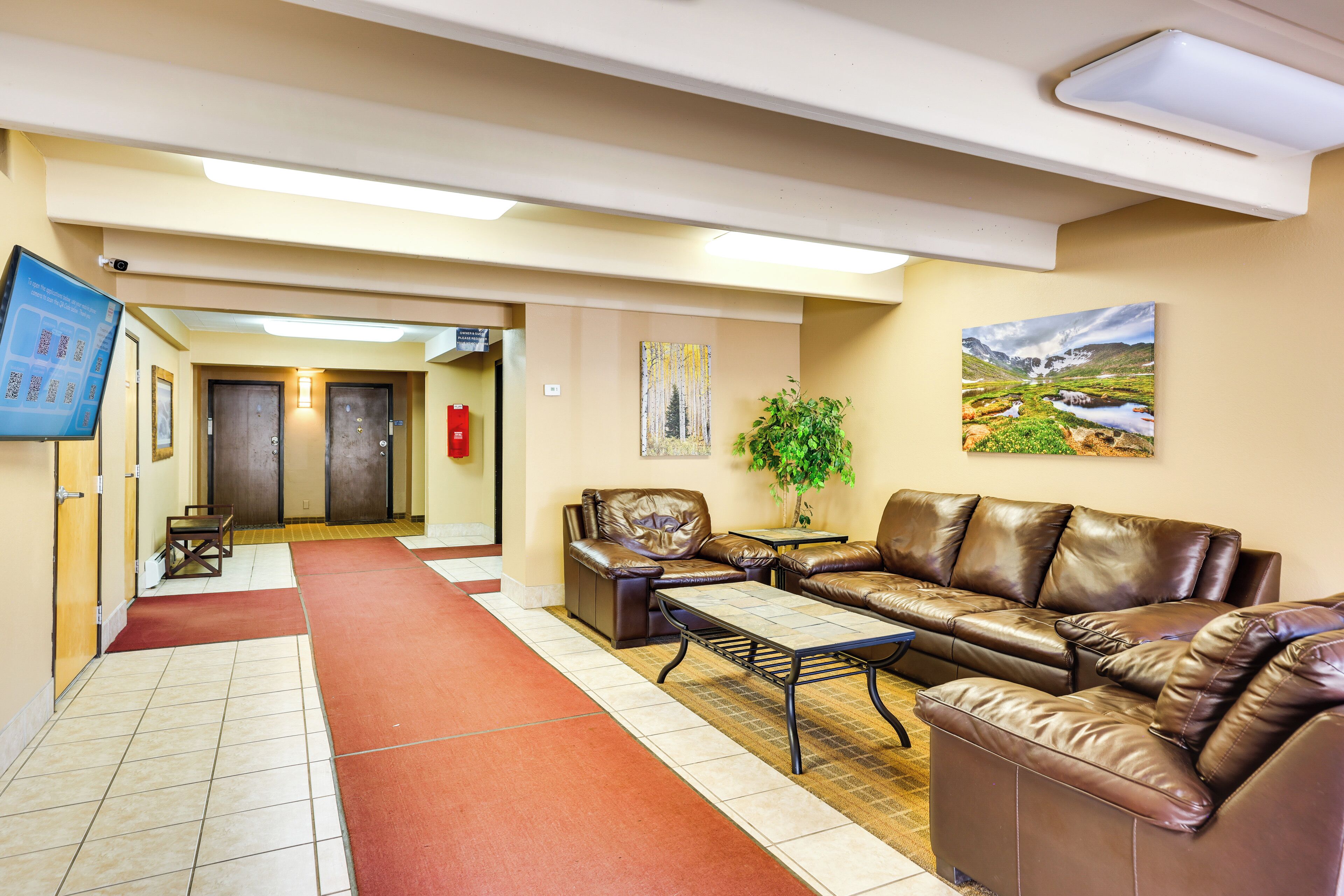 A hotel lobby with a reception desk, a brown leather sofa, a coffee table, and a painting on the wall.