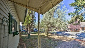 A covered porch with a garden area, a gravel path, and a view of a street with parked cars and trees.
