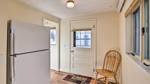 A hallway with a refrigerator, a door with a window, a chair, and a patterned rug.