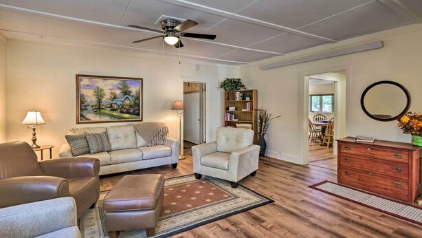 A living room with a sofa, armchairs, a coffee table, a fireplace, a ceiling fan, a bookshelf, and a mirror.
