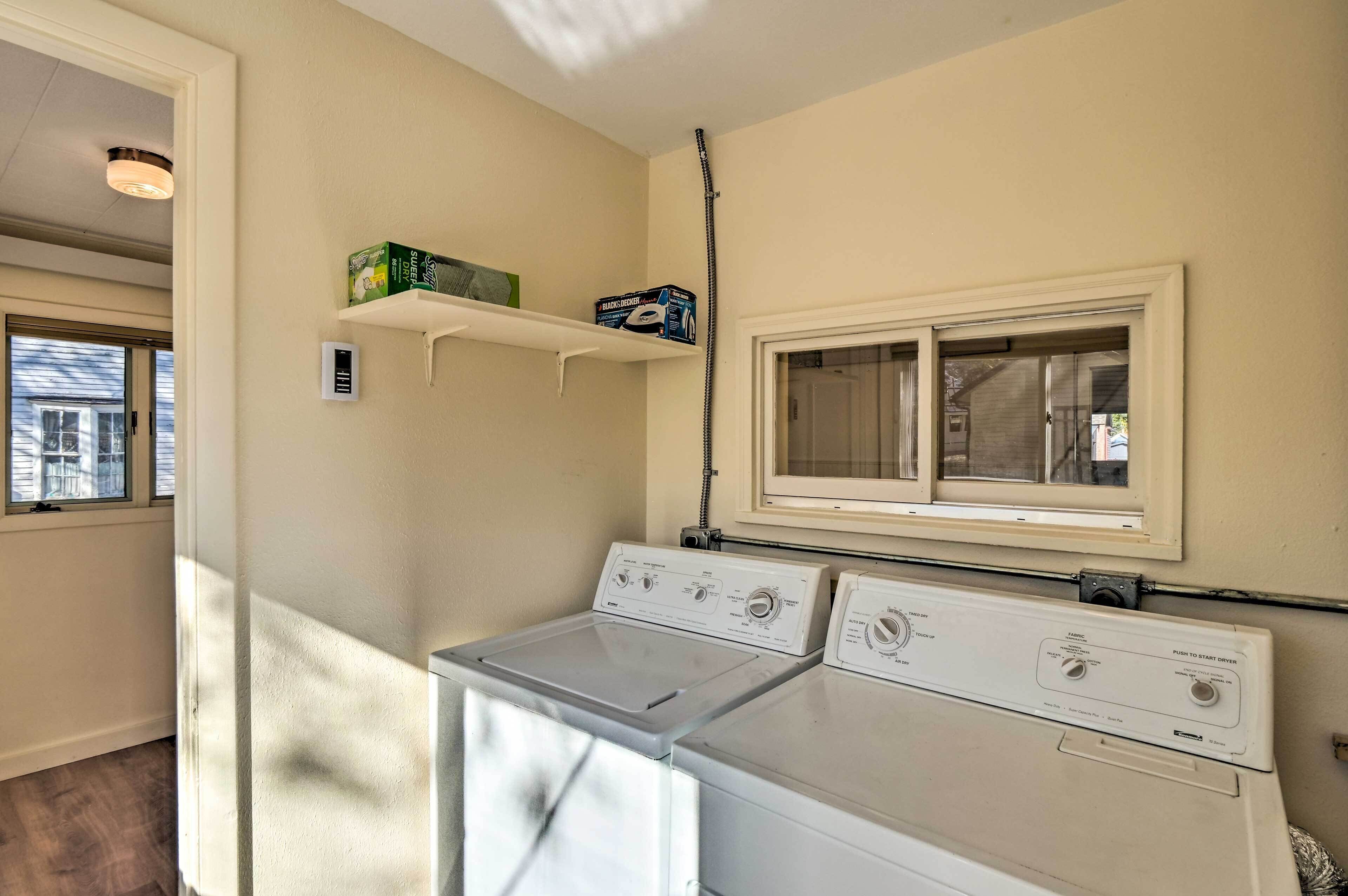 A laundry area with two white washing machines, a window above the machines, and a shelf with boxes.