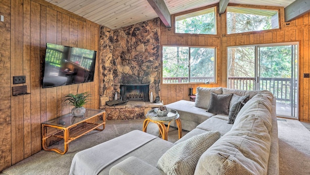 A cozy living room with a stone fireplace, wooden walls, a large TV, and a comfortable sofa. - Lake Arrowhead Cabin w/ Mid-century Charm! (Lake Arrowhead)