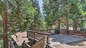 A wooden deck with a railing, surrounded by tall trees. - Lake Arrowhead Cabin w/ Mid-century Charm! (Lake Arrowhead)