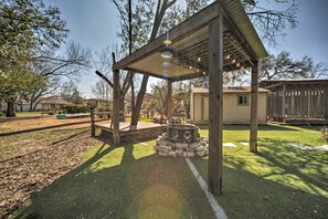 A wooden pergola with string lights, a stone fire pit, and a well-maintained lawn.